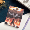 A7 Attack on Titan Shingeki no Kyojin tear-off memopad with dark dramatic anime cover art featuring Survey Corps imagery, on a clean aesthetic desk surface
