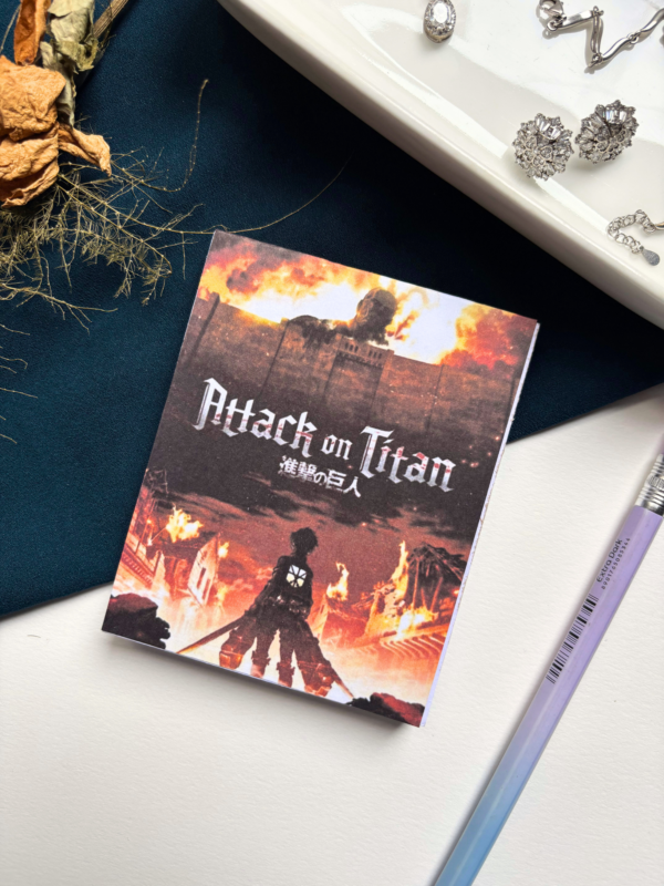 A7 Attack on Titan Shingeki no Kyojin tear-off memopad with dark dramatic anime cover art featuring Survey Corps imagery, on a clean aesthetic desk surface