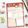 A5 daily planner with a terracotta cover featuring an illustrated bear and cottage design, including sections for date, goals, meal tracking, to-do list, and reminders.