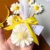 Handcrafted daisy-shaped candle with white petals and a yellow textured centre, wrapped in net with a customisable gift tag.