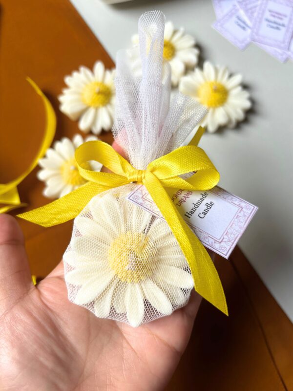 Handcrafted daisy-shaped candle with white petals and a yellow textured centre, wrapped in net with a customisable gift tag.