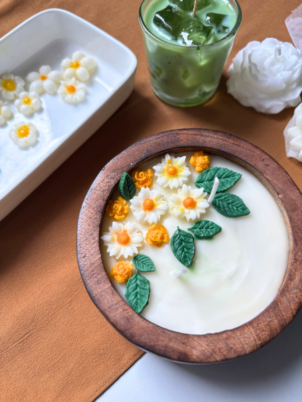 Handcrafted scented candle in a natural wooden bowl, topped with white and orange wax flowers and green leaves, with customisable wax colour and scent.
